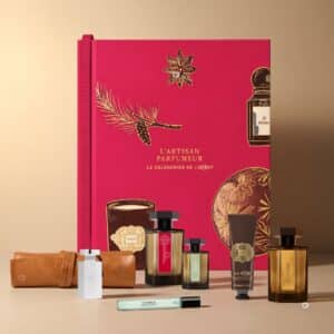 Luxus Adventskalender Parfum von L'Artisan Parfumeur 2026, aufgeklapptes Buch-Etui mit Flakons, Kerze und Lederaccessoires davor arrangiert