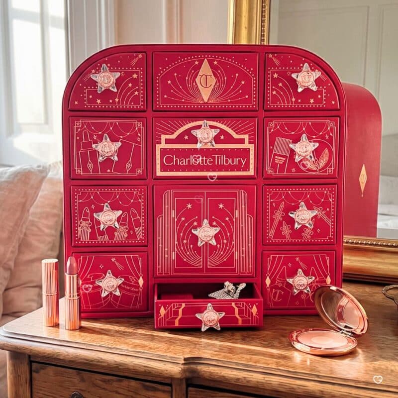 Charlotte Tilbury Adventskalender 2026 auf einer Holzkommode, ein Türchen geöffnet, daneben Lippenstift und Puderdose
