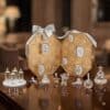 Swarovski Kristall Adventskalender 2026, geoeffnetes achteckiges Etui in Champagnerton mit davor aufgestellten Kristallobjekten, Adventskerzen und Kris Baer in weihnachtlichem Interieur