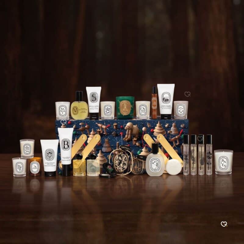 Diptyque Adventskalender 2026, Kerzen und Pflegeprodukte auf dunklem Holz
