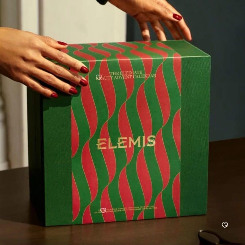 Hände halten die geschlossene Elemis Adventskalender-Box 2026, festliche Atmosphäre
