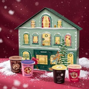 mymuesli Adventskalender 2026 mit vier 2go-Bechern vor dem verschneiten Adventskalenderhaus