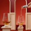 Flaviar Adventskalender 2026, Einschenken einer Probe in ein Glencairn-Glas vor roten Bögen