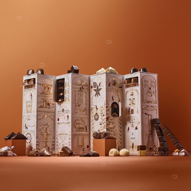 Neuhaus Adventskalender zum Teilen 2026, geöffnet mit 74 belgischen Pralinen vor terracottafarbenem Hintergrund