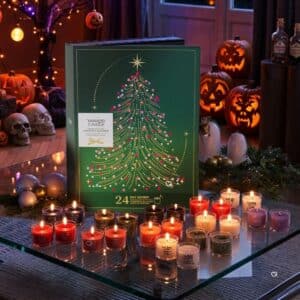 Yankee Candle Adventskalender 2026 mit Buch und brennenden Votivkerzen in weihnachtlicher Szene